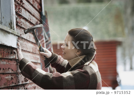 An organic farm in upstate New York, in winter. A woman with a hammer repairing the shingles on a barn.  9715352