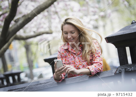 City life in spring. A young woman with long blonde hair sitting in a city park, looking at her smart phone.  9715432