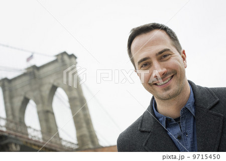 New York city, the Brooklyn Bridge crossing over the East River. A man looking at the camera and smiling.  9715450
