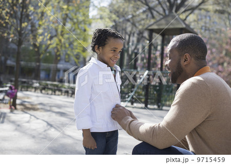 A New York city park in the spring. Sunshine and cherry blossom. A father kneeling and buttoning his son's jacket. 9715459