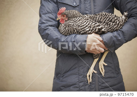 A woman wearing a grey coat and holding a chicken.  9715470