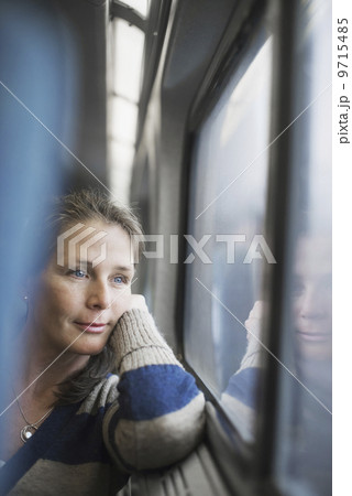 A woman sitting at a window seat in a train carriage, resting her head on her hand. Looking into the distance.  9715485