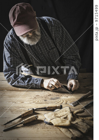 A man working in a reclaimed lumber yard workshop. Holding tools and sanding knotted and uneven piece of wood.  9715499