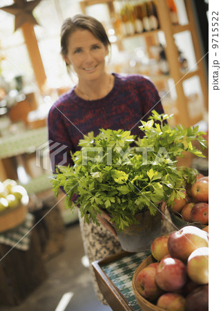 Organic Farmer at Work. A woman working ona farm stand, witha  display of fresh produce. Green plants and bowls of apples. 9715522