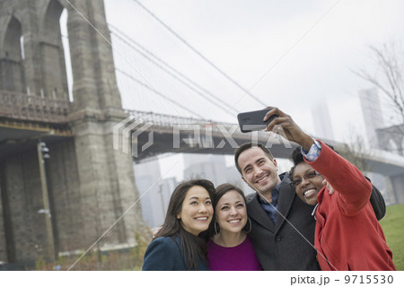 New York city. The Brooklyn Bridge crossing over the East River. Four friends taking a picture with a phone, a selfy of themselves. New York city. The Brooklyn Bridge crossing over the East River. Four friends taking a picture with a phone, a selfy of themselves. 9715530