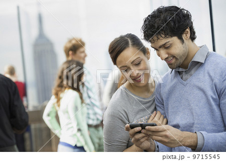 New York City. An observation deck overlooking the Empire State Building. A young couple taking photographs with a mobile phone. 9715545