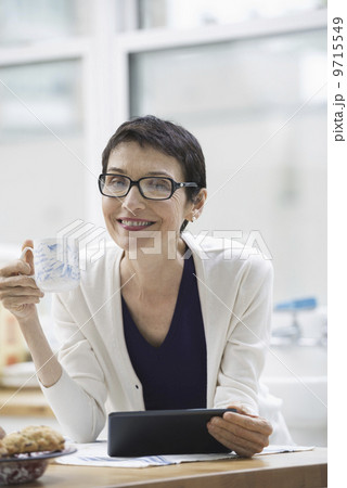 An office or apartment interior in New York City. A woman dressed for work in cream jacket, holding a cup of coffee. Checking her digital tablet. An office or apartment interior in New York City. A woman dressed for work in cream jacket, holding a cup of coffee. Checking her digital tablet. 9715549