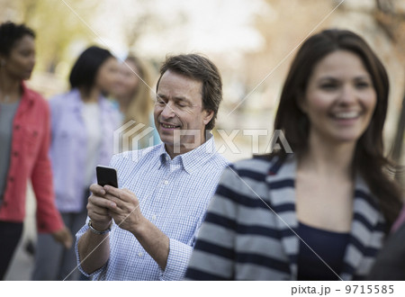 People outdoors in the city in spring time. A man checking his cell phone, among a group of men and women. People outdoors in the city in spring time. A man checking his cell phone, among a group of men and women. 9715585