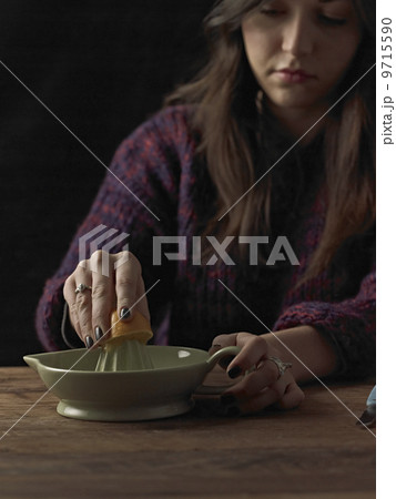 A woman holding a cut orange half, and using an orange squeezer to extract the juice, on a wooden table. 9715590