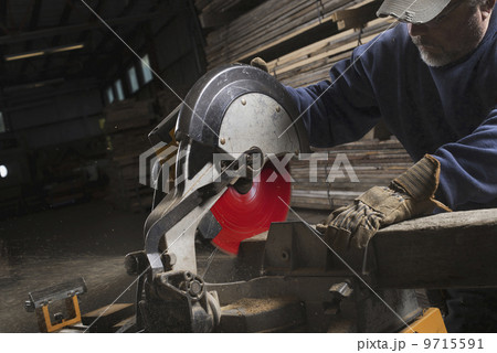 A reclaimed lumber workshop. A man in protective eye goggles using a circular saw to cut timber. A reclaimed lumber workshop. A man in protective eye goggles using a circular saw to cut timber. 9715591