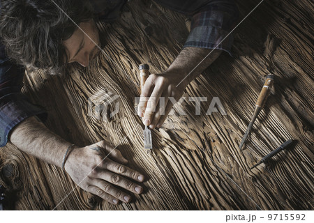 A man working in a reclaimed lumber yard workshop. Holding tools and sanding knotted and uneven piece of wood.  9715592