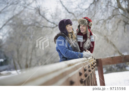 Winter scenery with snow on the ground. A couple, young man and young woman, leaning on a fence. Winter scenery with snow on the ground. A couple, young man and young woman, leaning on a fence. 9715598