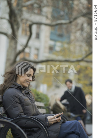 Woman seated in urban park with smartphone 9715664