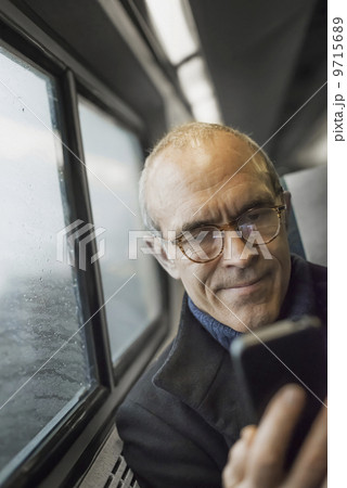 A mature man sitting by a window in a train carriage, using his mobile phone, keeping in touch on the move. A mature man sitting by a window in a train carriage, using his mobile phone, keeping in touch on the move. 9715689