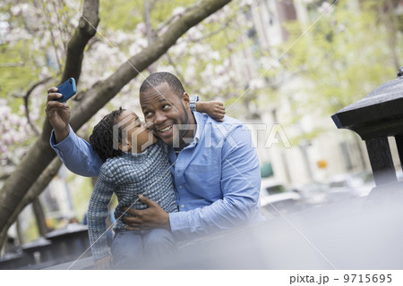 A New York city park in the spring. Sunshine and cherry blossom. A woman taking a picture of herself and her son with a smart phone. 9715695