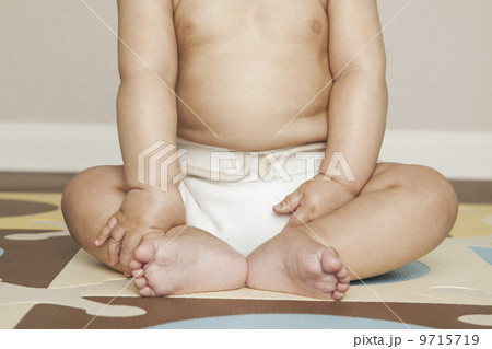 A young 8 month old baby boy wearing cloth diapers, sitting on the floor. A cot blanket over his head. 9715719