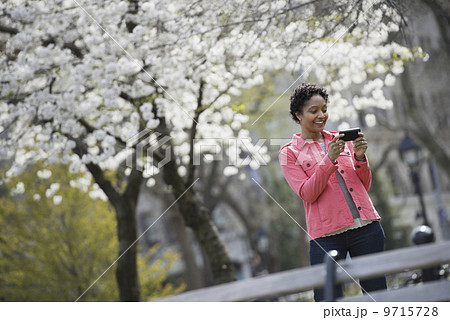 Outdoors in the city in spring time. New York City park. White blossom on the trees. A woman holding her mobile phone and smiling. Outdoors in the city in spring time. New York City park. White blossom on the trees. A woman holding her mobile phone and smiling. 9715728