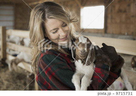 A woman cradling a young goat kid in her arms, on a farm. 9715731