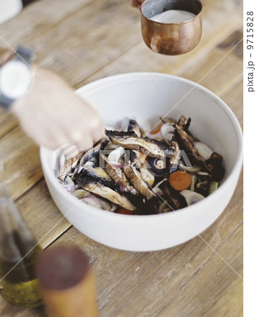A domestic kitchen. A bowl of fresh chopped vegetables, in a white bowl. A person's hand mixing and applying a dressing. 9715828