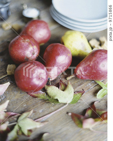 A domestic kitchen tabletop. A small group of fresh organic pears and a stack of white plates.   9715866