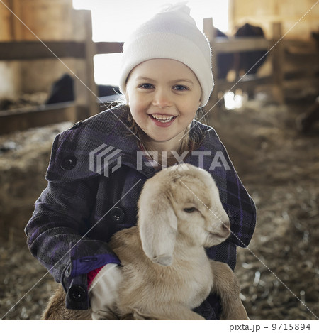 A child in the animal shed holding and stroking a baby goat.   9715894