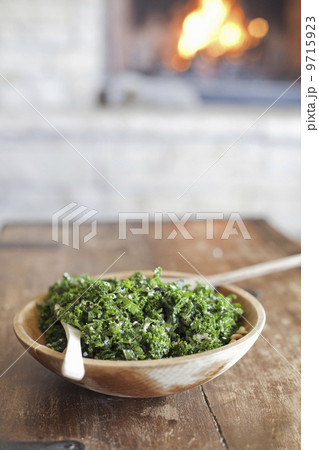 A tabletop with a log fire in the background. Green leafy salad in a wooden bowl. 9715923