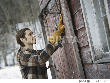 An organic farm in winter in New York State, USA. A man with a hammer, mending a barn door. 9716052