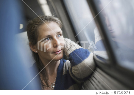 A woman sitting at a window seat in a train carriage, resting her head on her hand. Looking into the distance. A woman sitting at a window seat in a train carriage, resting her head on her hand. Looking into the distance. 9716073