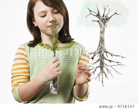 A young girl holding a small evergreen seedling to her nose and smelling it. An illustration of the plant with roots on a clear seethrough surface.  9716147