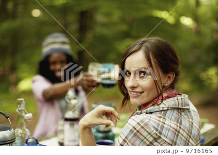 Two young woman drinking a toast at a picnic site or campsite in the woods.  9716165
