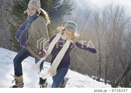 Winter scenery with snow on the ground. A woman and a child hand in hand running across the snow. 9716247