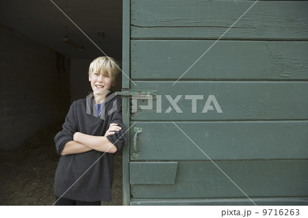 A boy leaning against a wooden barn door, at an animal sanctuary.  9716263