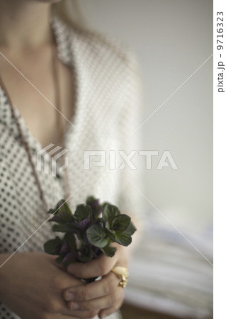 A woman wearing a dress and necklace, holding a small bunch of red and green plant leaves. Cologne mint leaves.  9716323