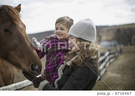 A woman and child patting a horse in a paddock on a farm. 9716467
