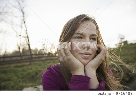 A young girl with her chin in her hands, leaning on a fence at an animal sanctuary.  9716488
