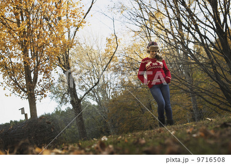Autumn foliage on the trees on a farm. A young girl in a red knitted jumper with a warm tartan woolly hat.  9716508