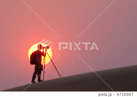 Photographer silhouetted in the setting sun in the Namib Desert, Namibia 9716907