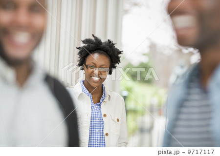 Outdoors in the city in spring. An urban lifestyle. A woman looking at the camera, with two men in the foreground. 9717117