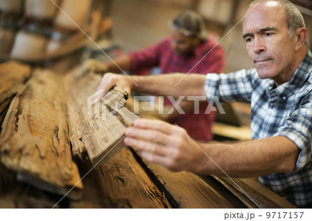 A reclaimed lumber workshop. A group of people working. A man measuring and checking planks of wood for re-use and recycling. A reclaimed lumber workshop. A group of people working. A man measuring and checking planks of wood for re-use and recycling. 9717157