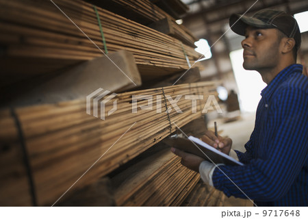 A heap of recycled reclaimed timber planks of wood. Environmentally responsible reclamation in a timber yard. A man with a clipboard by a rack of planks. 9717648