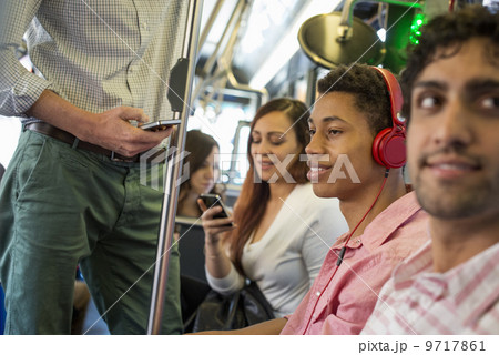 Urban Lifestyle. A group of people, men and women on a city bus, in New York city. A man with headphones on. A man and a woman checking their smart phones. 9717861