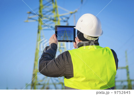 Electrical Engineer with tablet PC near High voltage tower 9752645