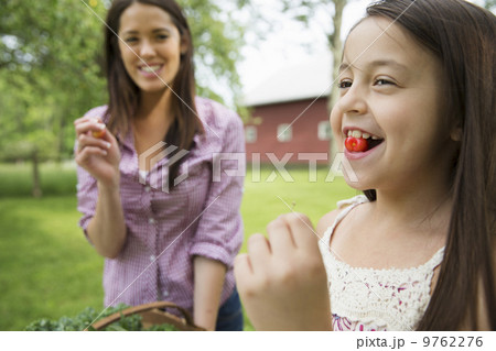 A summer family gathering at a farm. A child with a fresh cherry between her teeth. A young woman watching her and laughing. 9762276