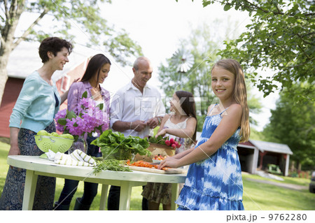 A summer family gathering at a farm. A table laid with salads and fresh fruits and vegetables. Parents and children. Two girls, one young woman and a mature couple. 9762280