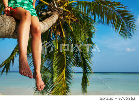Woman sitting on a palm tree at tropical beach 9765862