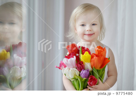 Adorable toddler girl with tulips by the window Adorable toddler girl with tulips by the window 9775480