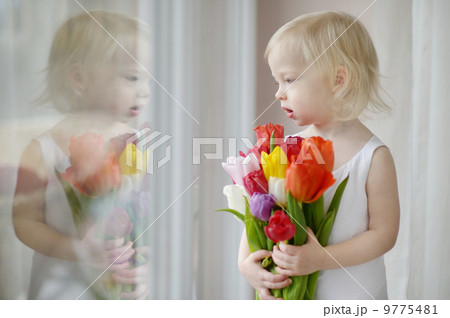 Adorable toddler girl with tulips by the window Adorable toddler girl with tulips by the window 9775481