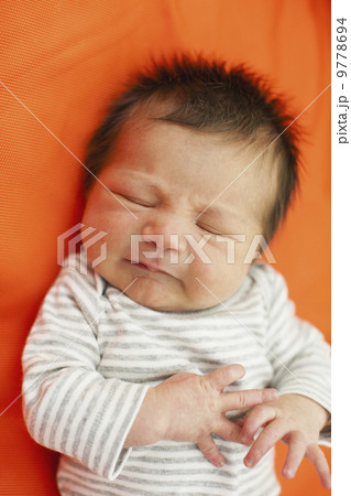 A baby in a striped top with his eyes closed, lying on an orange pillow. 9778694