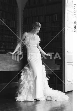 A woman wearing an elegant floor length gown with a full skirt, decorated with feathers. A woman wearing an elegant floor length gown with a full skirt, decorated with feathers. 9778771