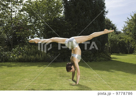 A young woman doing a splits handstand on the grass in a garden. A young woman doing a splits handstand on the grass in a garden. 9778786
